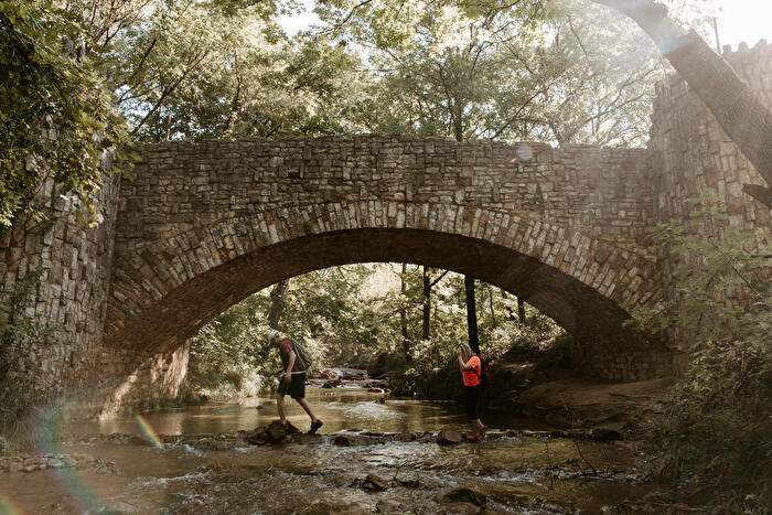 Couple hiking and crossing creek under bridge in Chickasaw Country