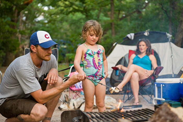 Family camping around campfire roasting marshmallows